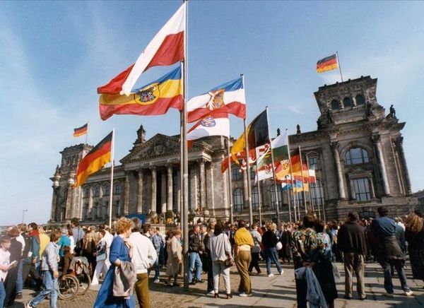 Bild des Reichstages am 3. Oktober 1990 in Berlin: Um die schwarz-rot-goldene Fahne gruppieren sich vor dem Reichstagsgebäude die Fahnen aller Bundesländer Deutschlands.
